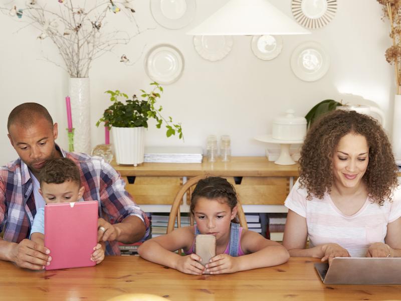 Family Sitting Around Table At Home Using Technology