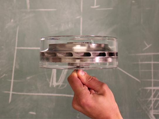 A hand holds a cylindrical metal part almost entirely encased in a cylindrical block of crystal-clear ice.