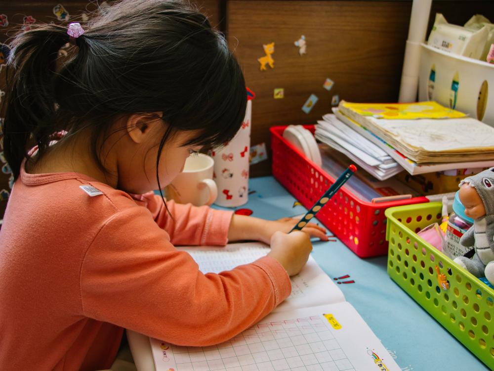 Young girl with black pony tail and orange shirt completing worksheet