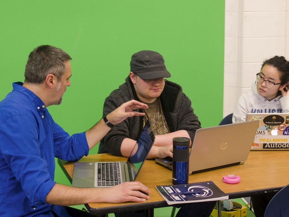 Kenan Zekic and students sit talking in front of a green screen