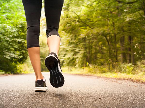 The feet and legs of a woman walking on a path surrounded by woods.