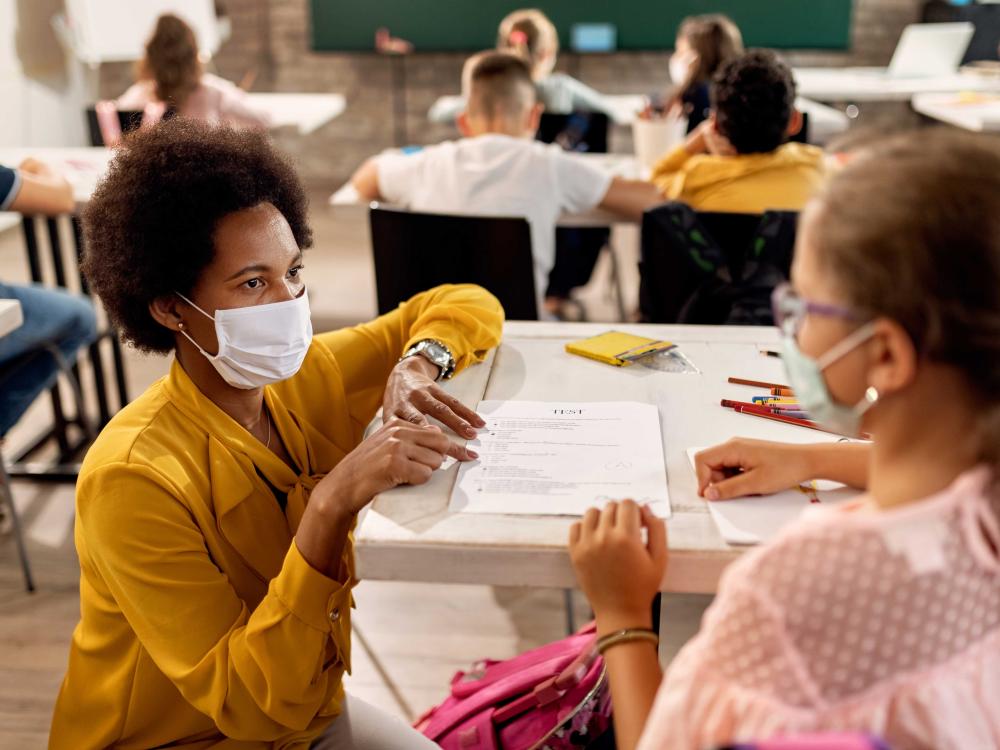 Masked teacher and student at desk