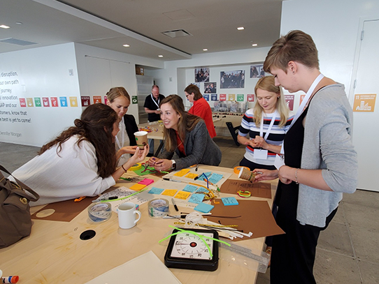 Five people stand around a table covered in Post-its, pipecleaners and cardboard. 