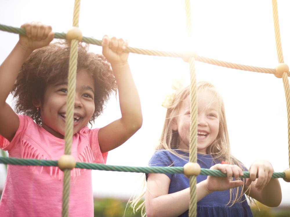 Two small children smiling and climbing on a rope course