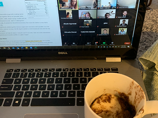 Coffee mug with cake sits near a laptop featuring a Zoom call. 