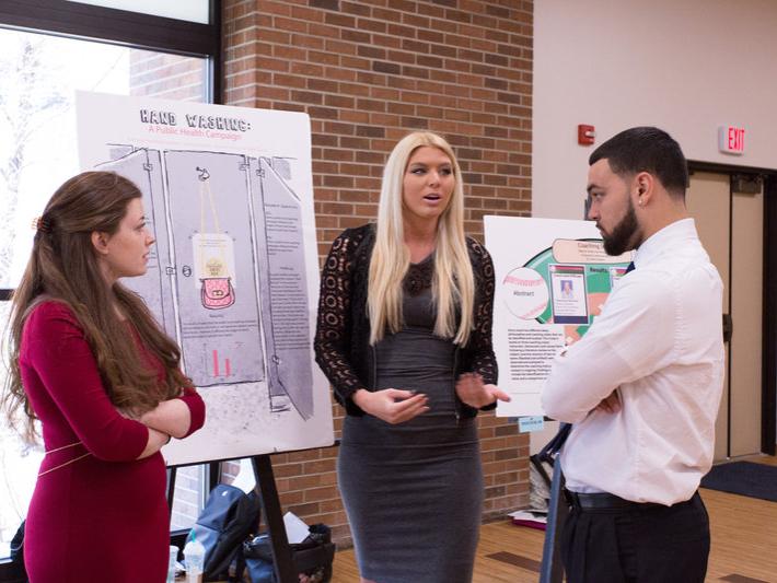 Three students gather around a posterboard to discuss their research.