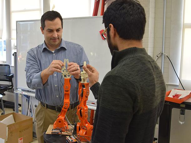 Alan Wagner, assistant professor of aerospace engineering, and graduate student Sagar Lakhmani adjust a pair of Braccio robotic arms on the latest generation of emergency evacuation robots.