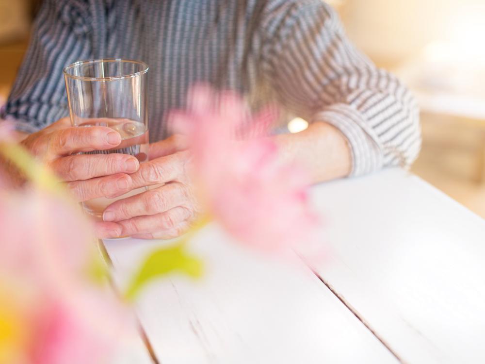 Close up photo of an older person's hands holding a glass of water