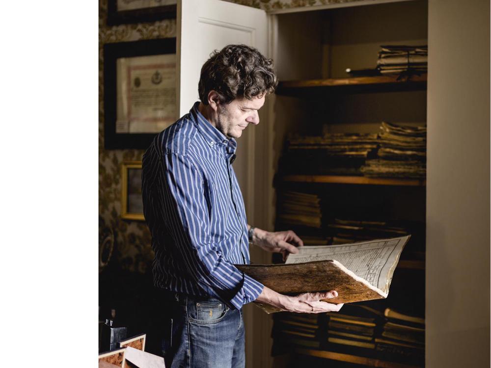 Man holding an old ledger listing grape production in front of a closet containing 200 years worth of ledgers