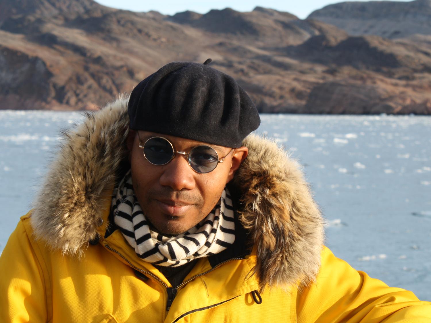 Paul D. Miller (aka DJ Spooky) poses in front of mountainous land formations in the Arctic.