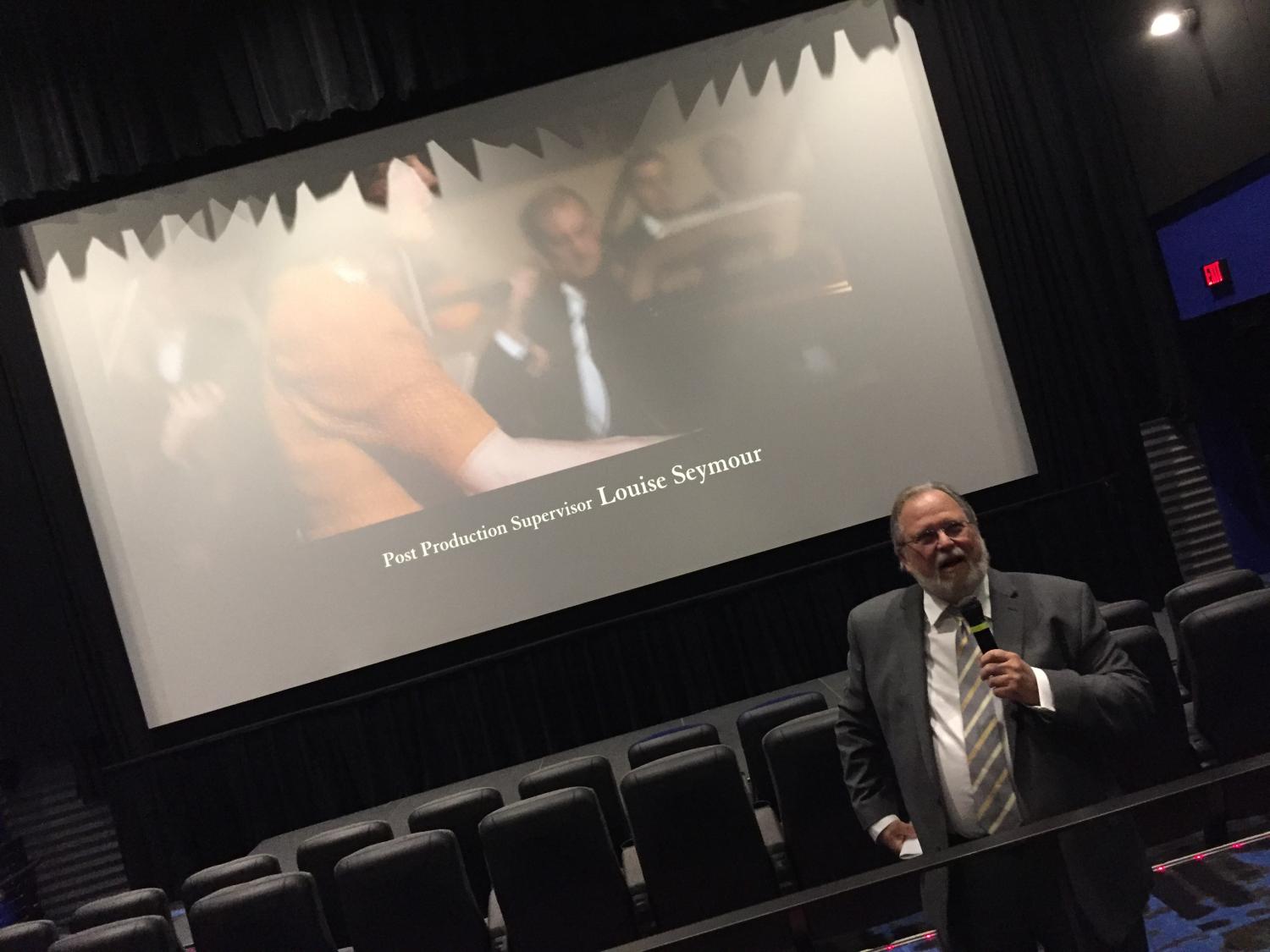 A man speaks in front of a movie screen