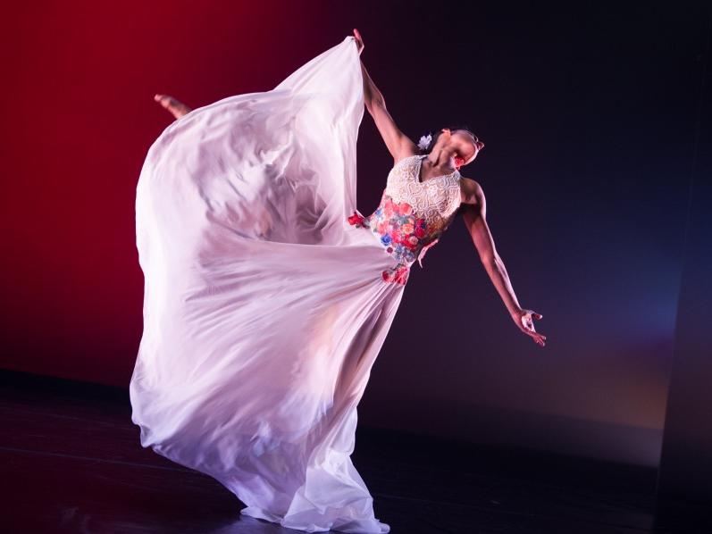 A dancer wears a gauzy dress and outstretches her arms.
