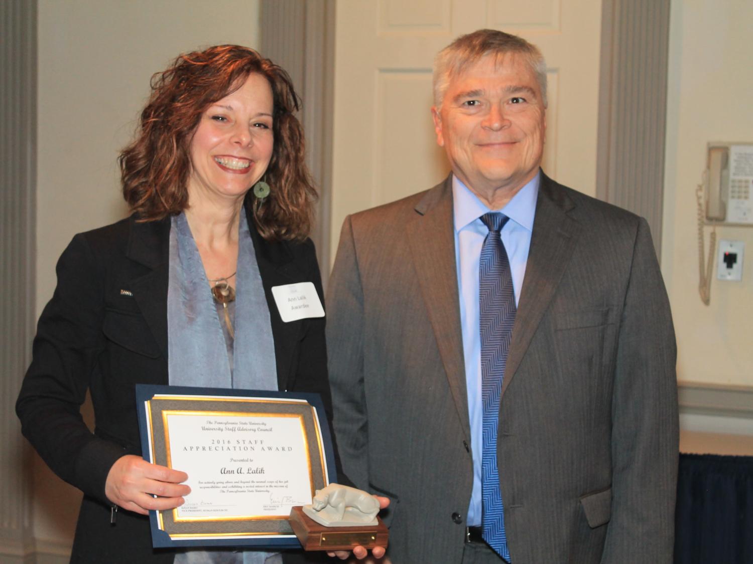 Two people stand with award