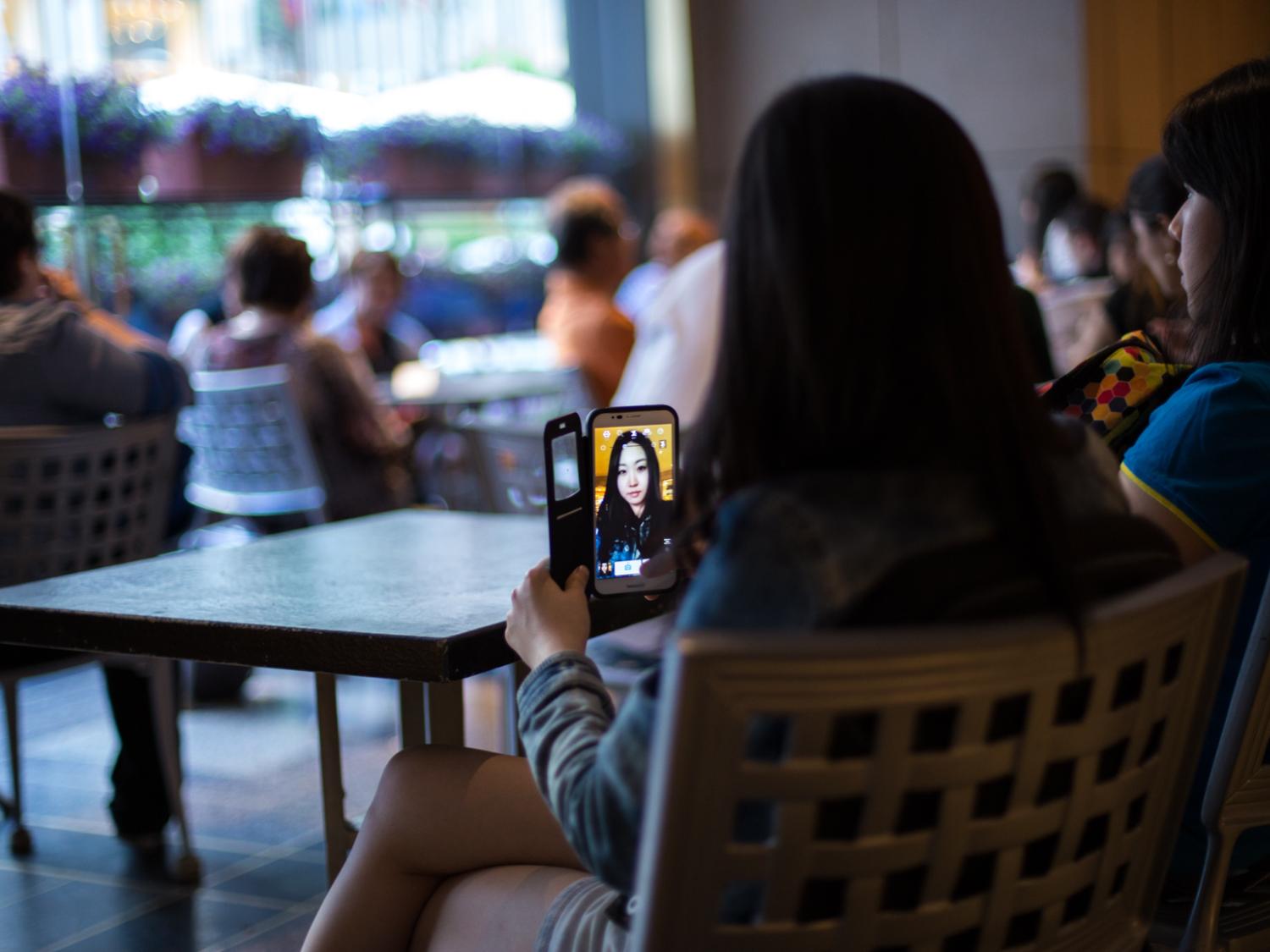 Young woman sits in a chair and takes a selfie with a smartphone.