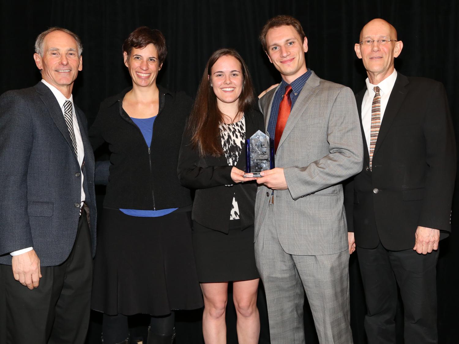 Two Penn State students holding award, flanked by advisors and competition staff 
