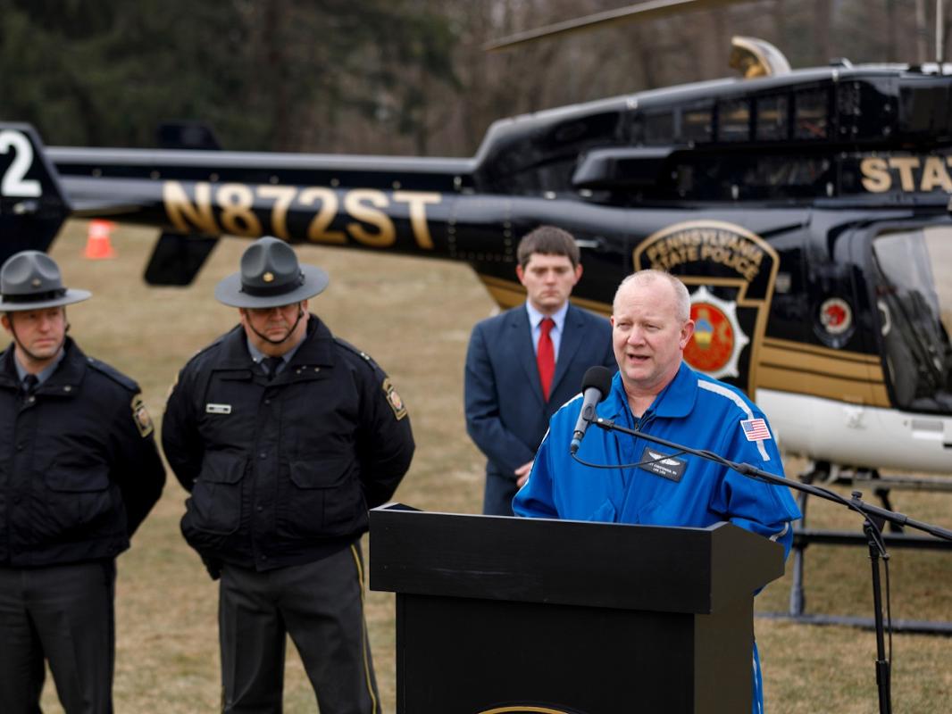 A man speaks at a podium in front of a helicopter