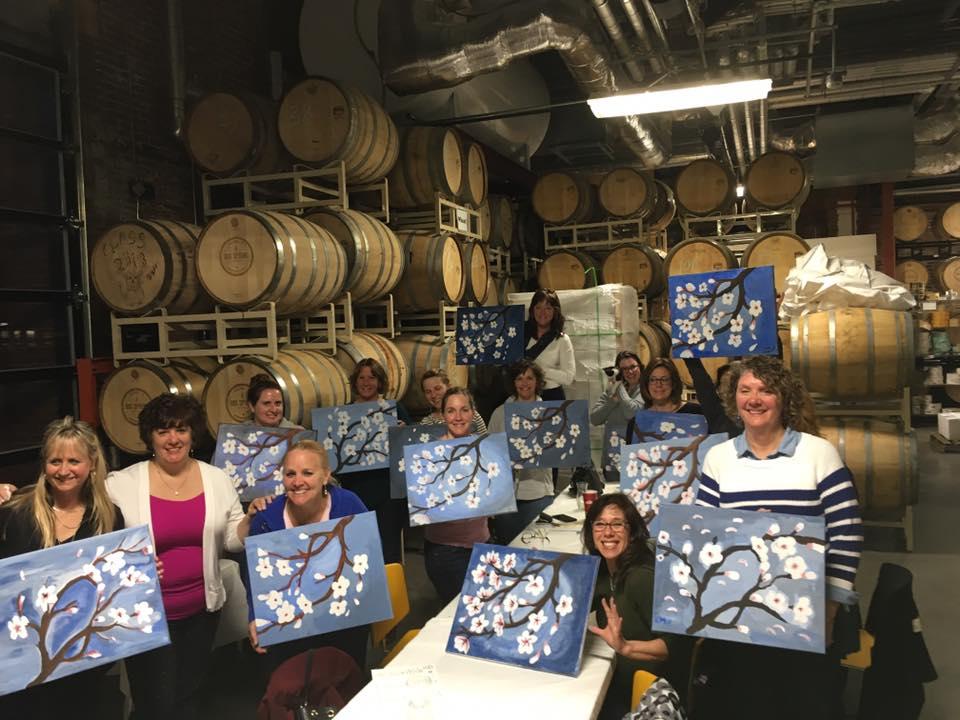 Staff members hold up their artwork at the Sip and Paint event.