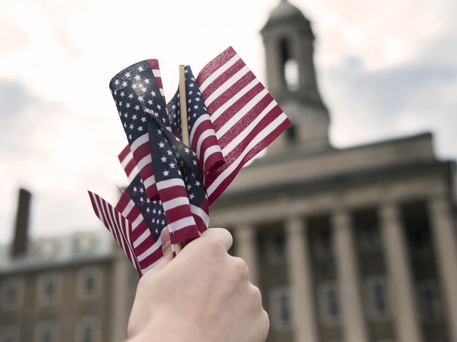 A person holds a group of mini American flags in front of the Old Main building on Penn State's University Park campus.
