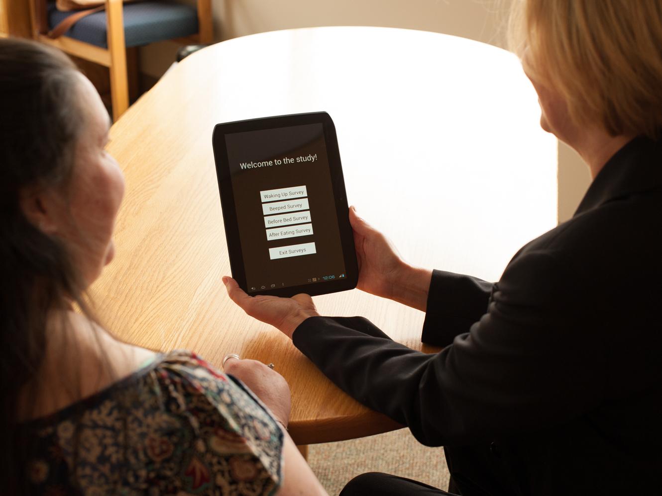 Two people look at a survey on a mobile tablet
