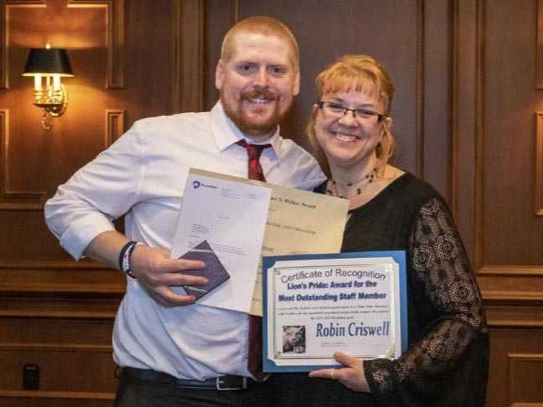 A young man and woman stand together with certificates in hand.