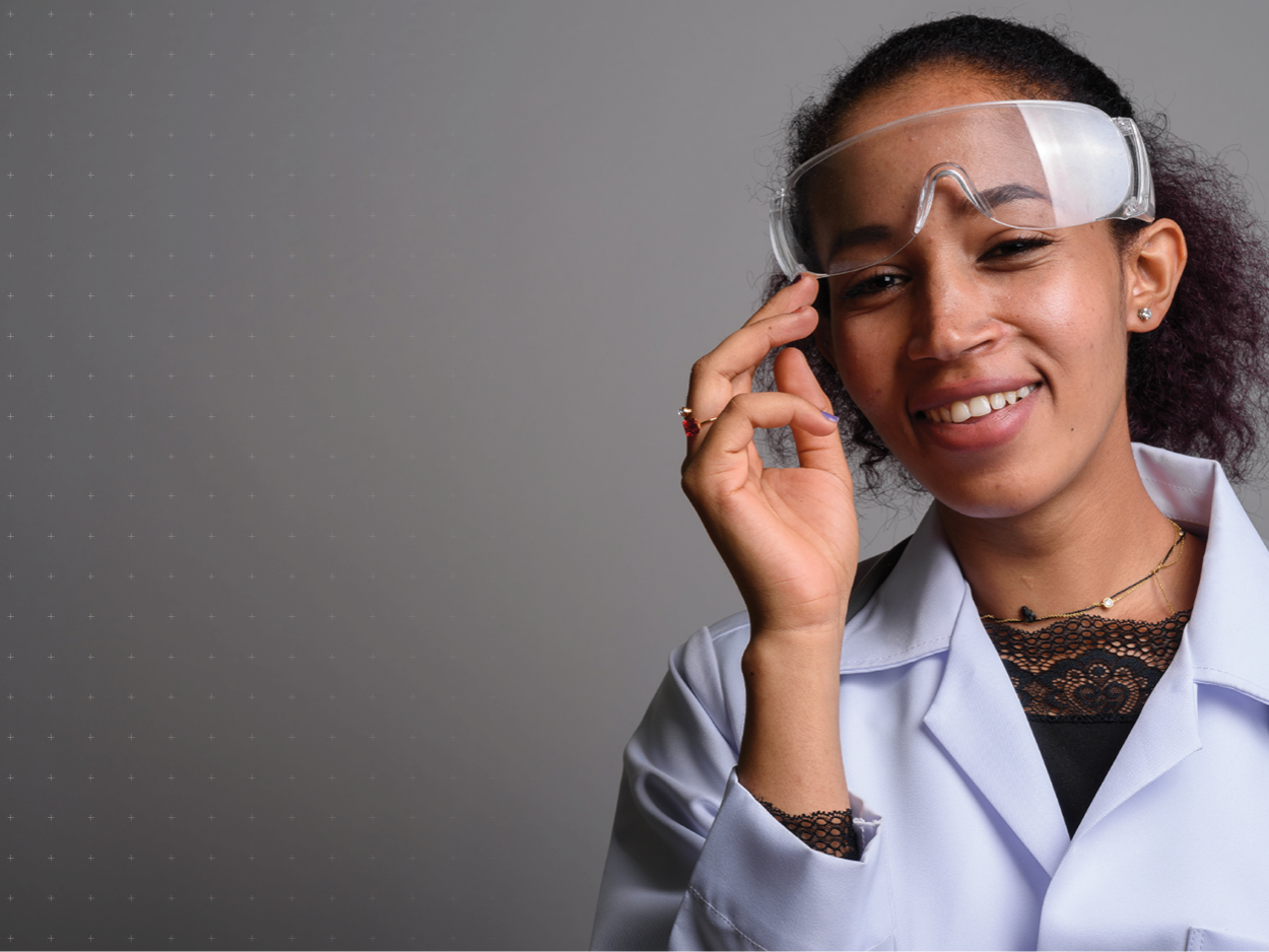 Smiling teenager wearing a lab coat and protective goggles.