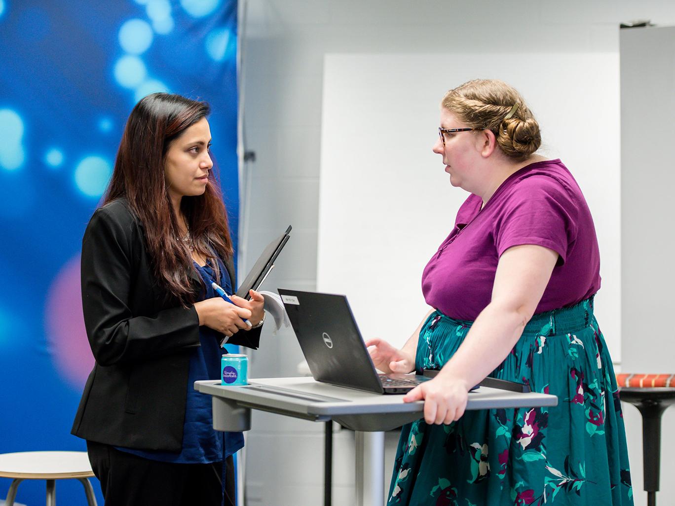 two women in a conference room speaking at a lectern