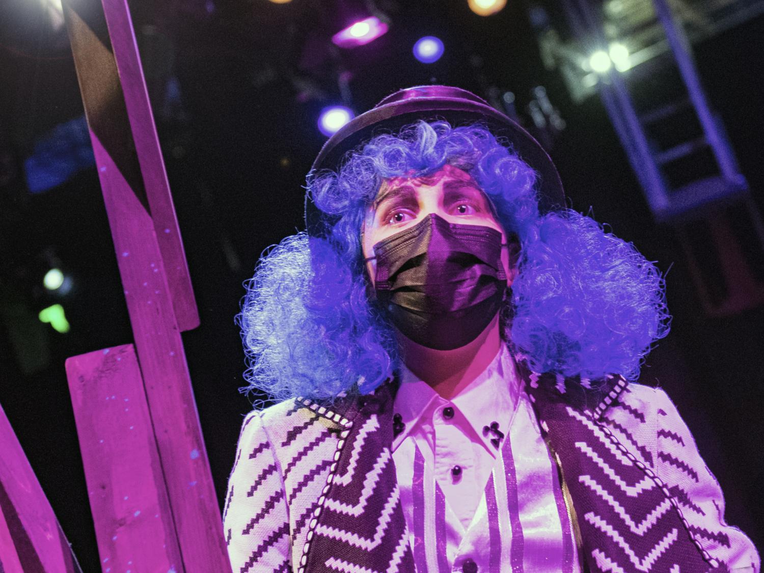 A person with a purple wig, mask and outfit on a stage