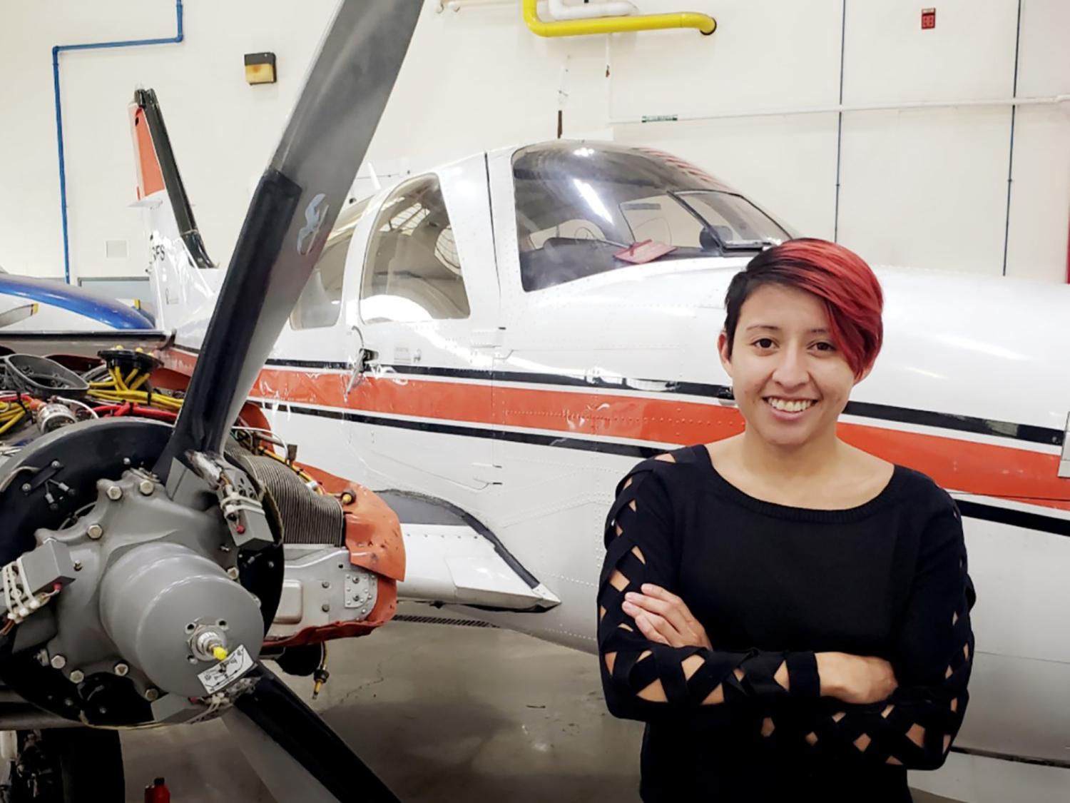 Alicia Martinez standing in front of a small white and orange airplane