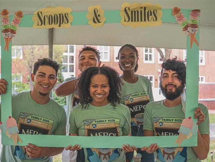 A group of students hold a paper frame with the phrase "Scoops & Smiles". 