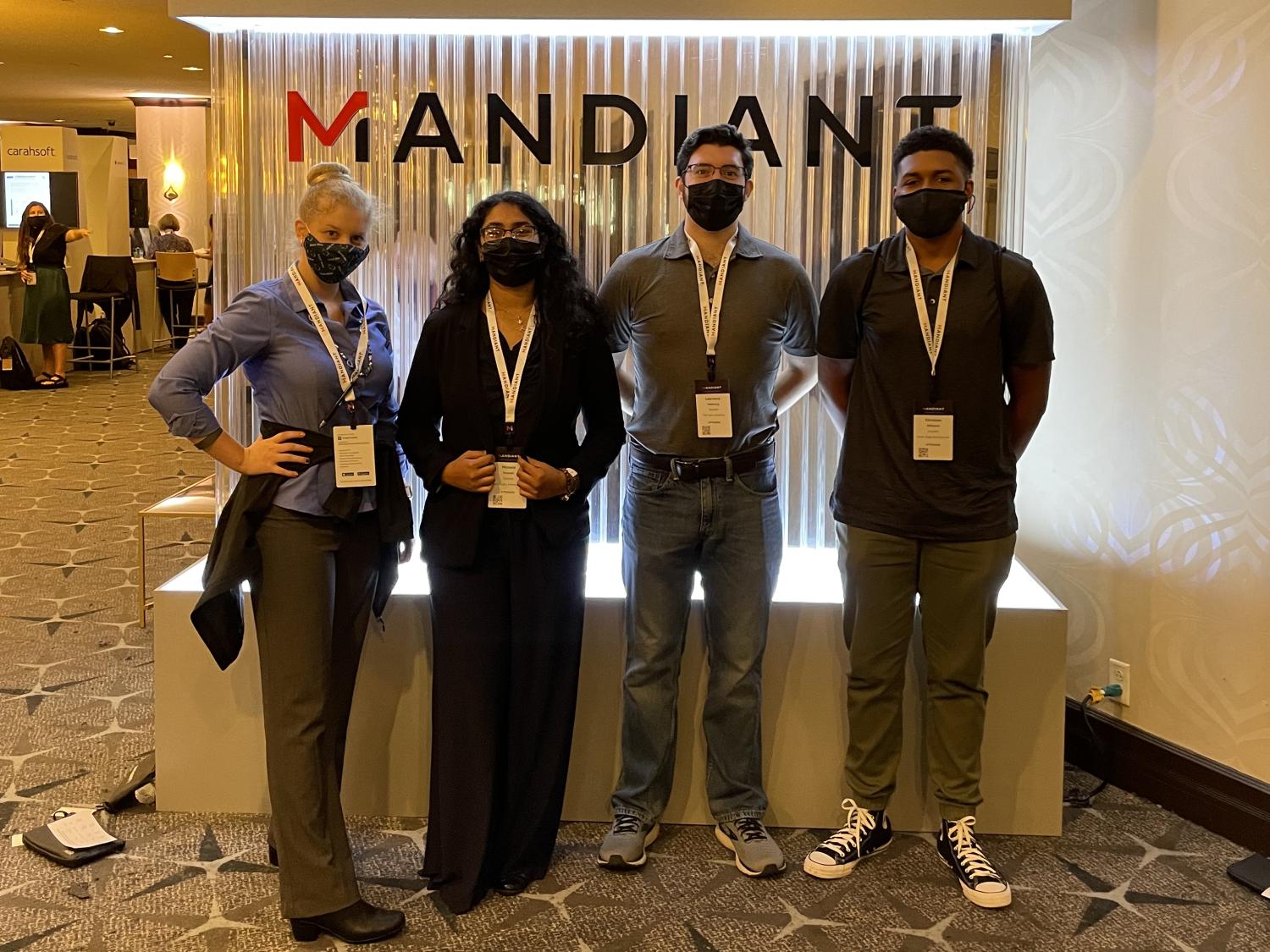 Four students standing in front of a vendor booth in a large conference room.