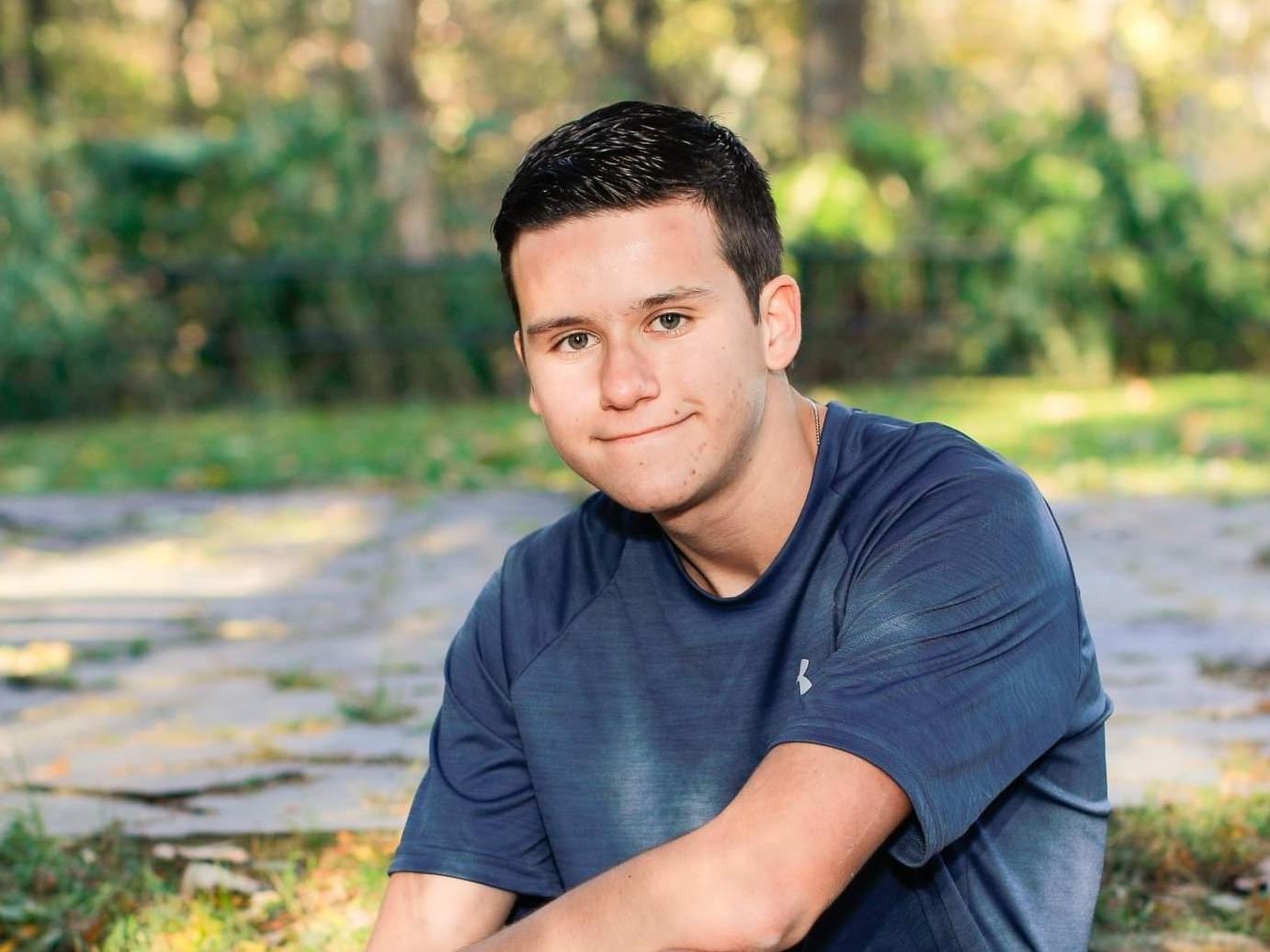 Male student seated outdoors on a rock wearing shorts and a T-shirt.