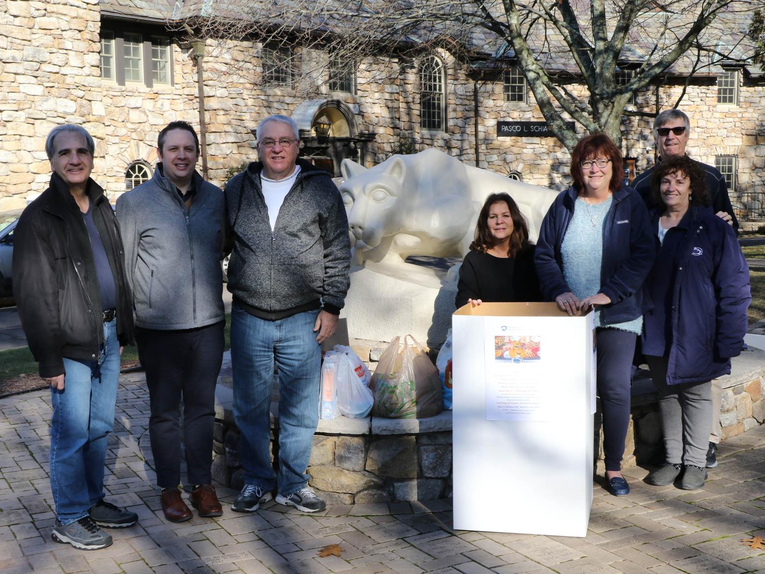 Group of men and women lined up outside in front of Nittany Lion statue and cardboard box full of food donations.