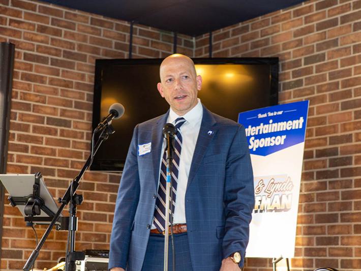 A man in a dark blue suit stands on a stage at an event