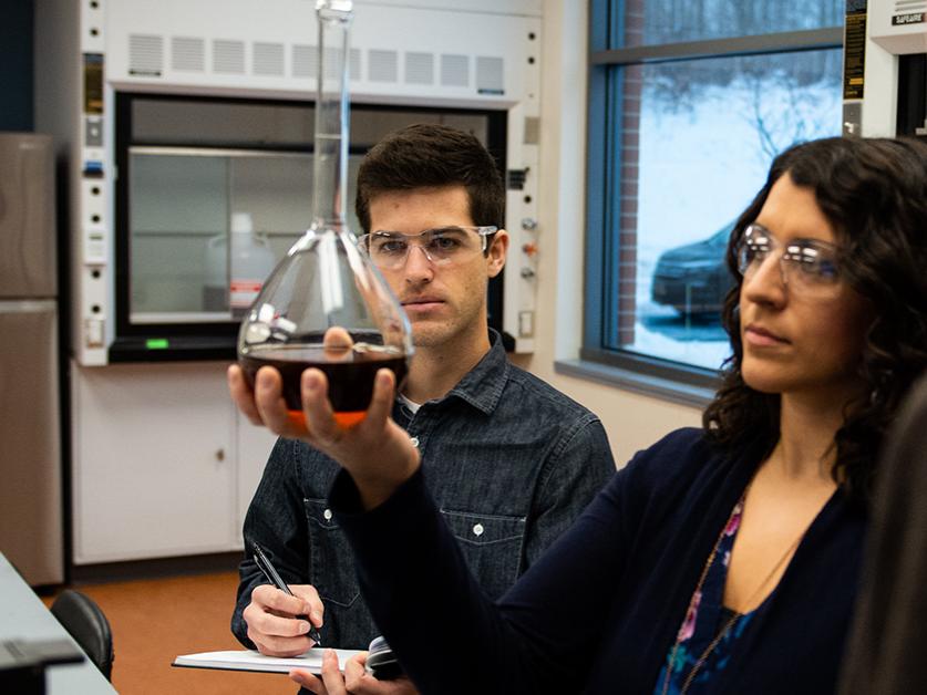 Two researchers examine a liquid in a beaker while working in a chemistry lab at Penn State Behrend.