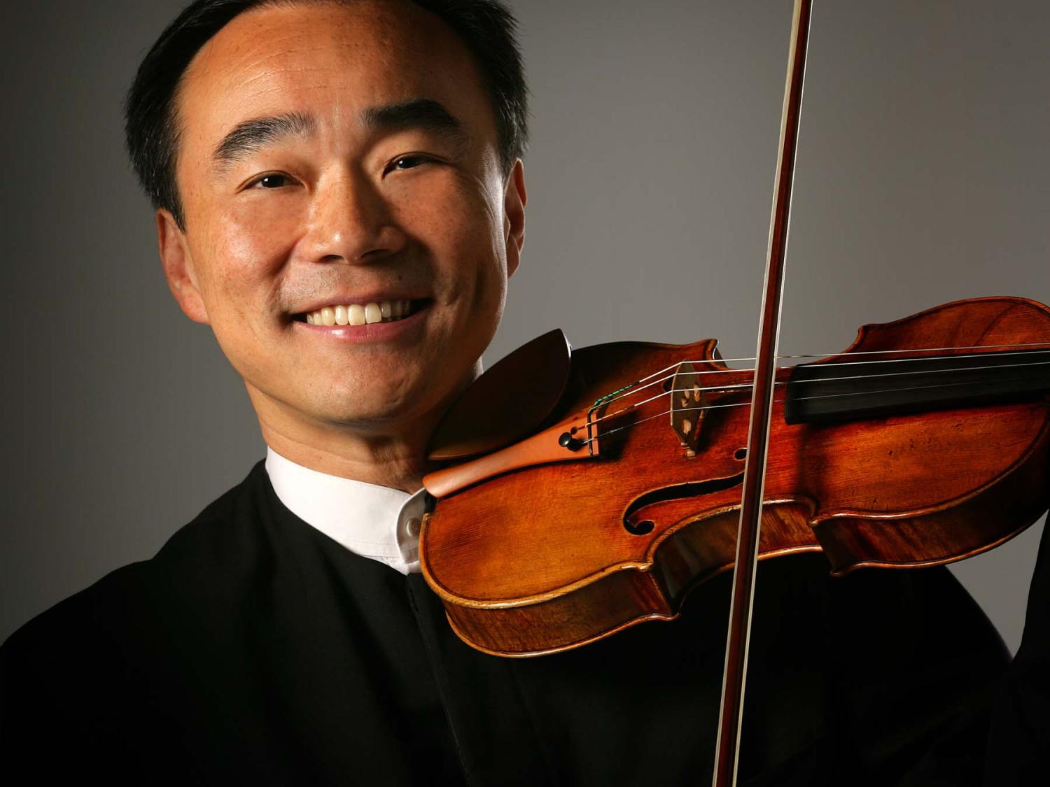 A man rests a violin on his shoulder and smiles.