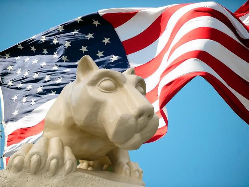 A Nittany Lion statue in the foreground, with an American flag waving in the background.