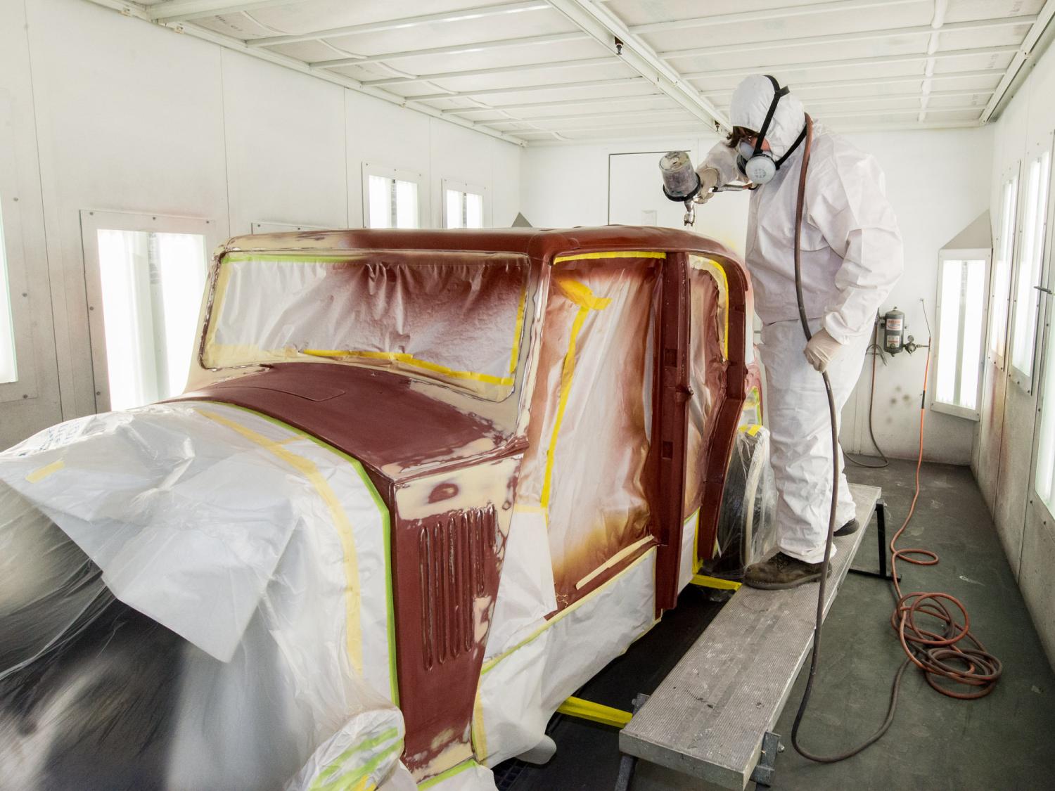 A student paints a vintage Rolls Royce automobile in a paint shop bay.