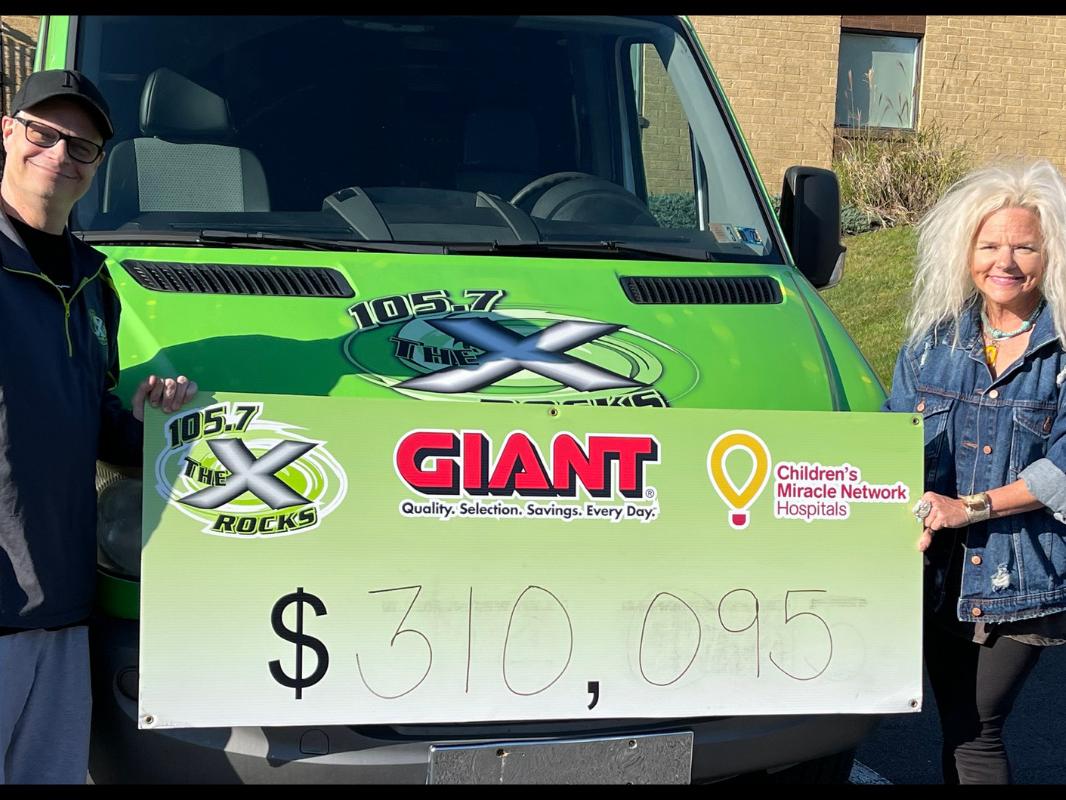 Nipsey and Jen Shade from The People’s Morning Show on WQXA 105.7 The X stand in front of a station vehicle, holding a sign that has the amount $310,095 on it.