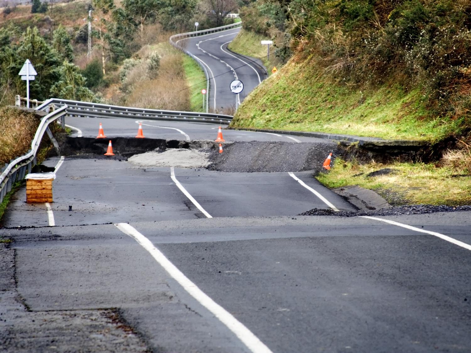 A damaged road shows sections that are cracked and missing.