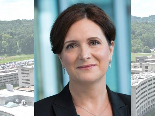 Jody Reyes is in a professional headshot over a background with vertical bars. She has straight hair pulled back and is wearing a jacket, necklace and earrings. Her headshot is over an aerial image of the Hershey Crescent building.