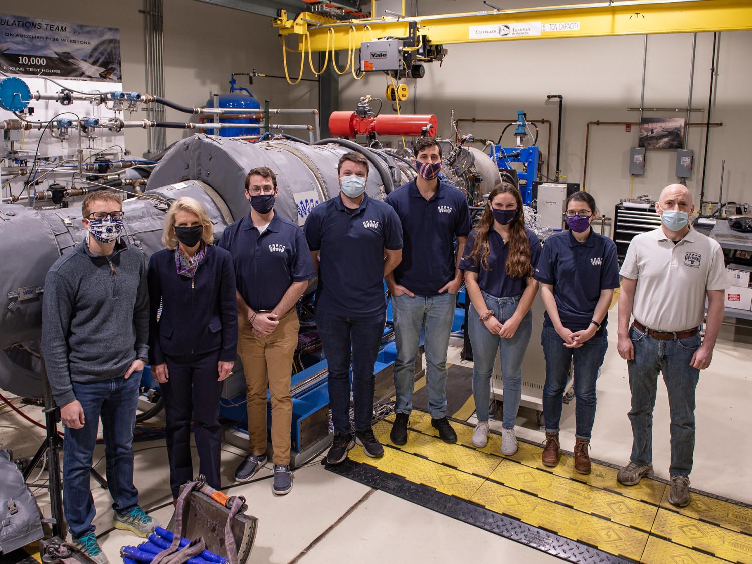 A team of researchers working on sustainable aircraft pose in front of a gas turbine engine. 