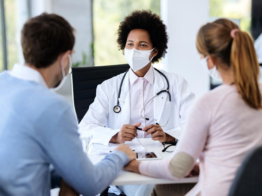 A doctor wearing protective face mask meets with a couple at a clinic.
