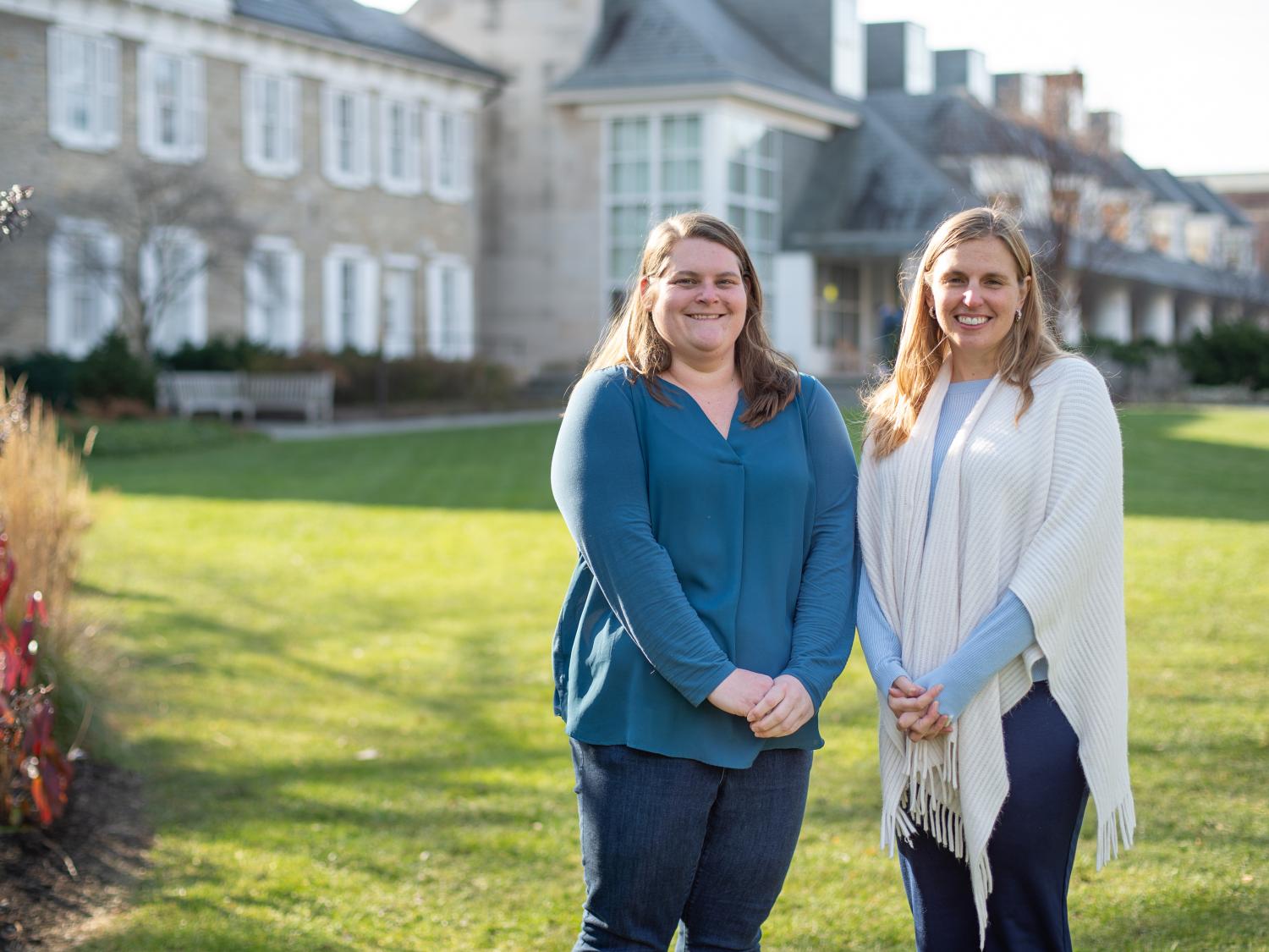 Two women wearing sweaters smile and pose outdoors. 