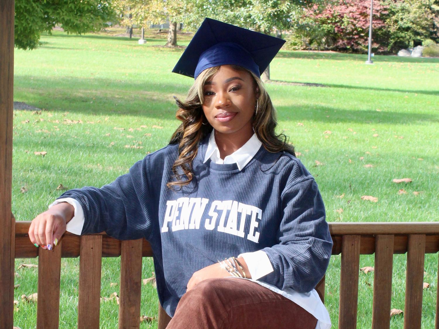 A students wearing a graduation cap sitting on an outside bench.