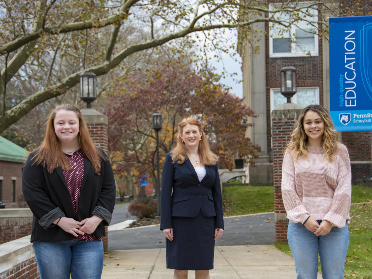 An image of two female students and professor with campus mall walk behind them.