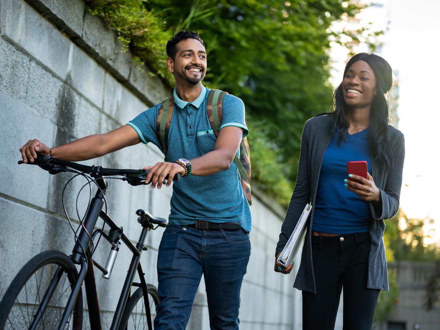 Young man pushing bike walking next two young woman carrying a binder and a smartphone