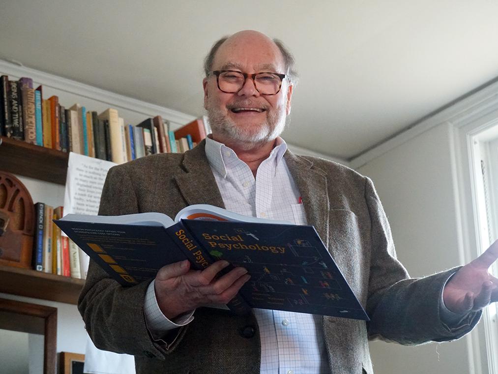 Man holding open text book standing in front of book shelf