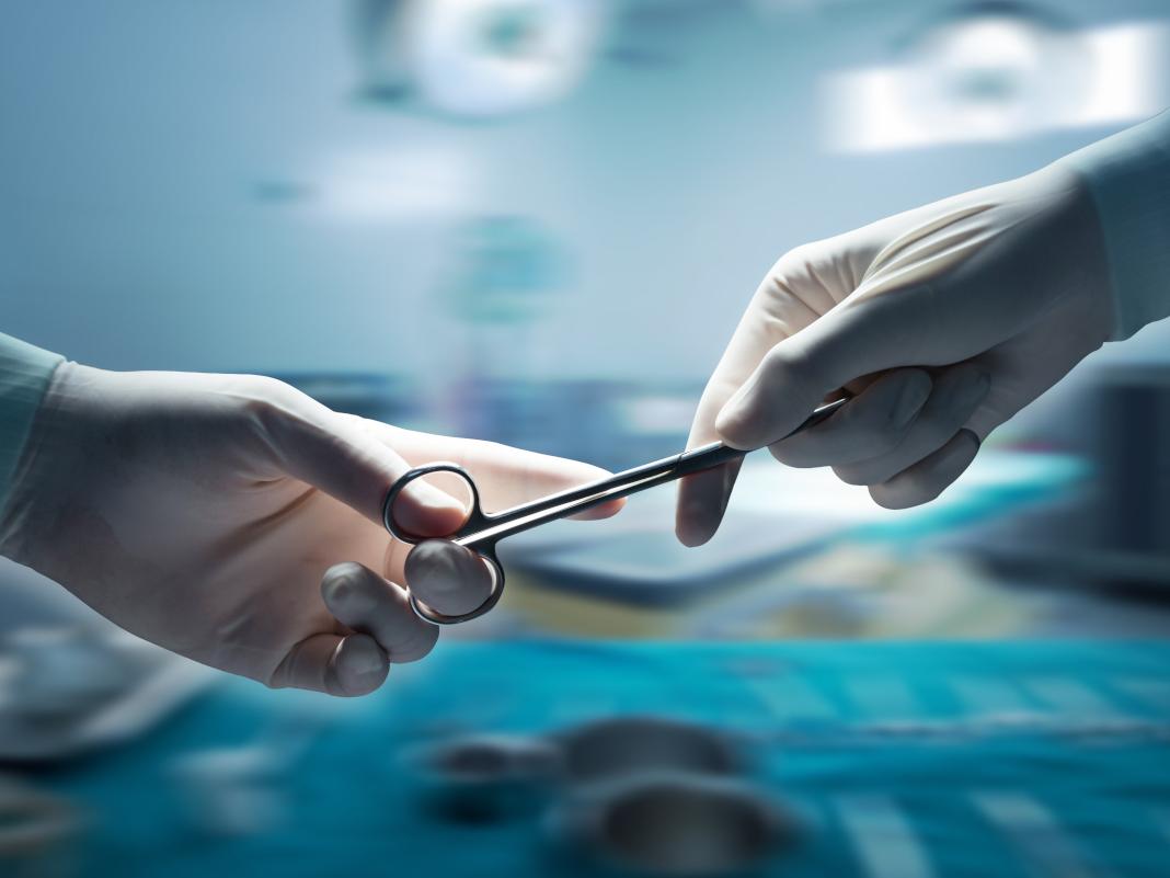Close-up of two gloved hands handing off a piece of equipment in an operating room.