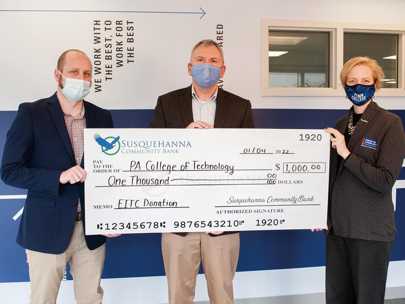 Three people hold up a large check