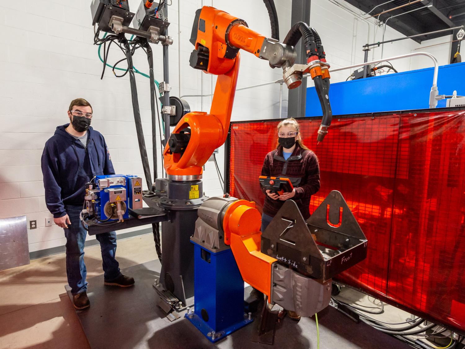 Two students stand next to an orange robot and controller